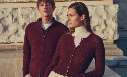 Two people wearing matching red cashmere outfits standing in front of a stone building