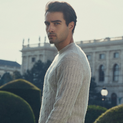 Man wearing a N.Peal sweater standing in front of a building with a blurred background