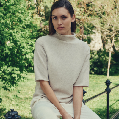 Woman wearing a N.Peal sweater sitting outdoors with greenery in the background